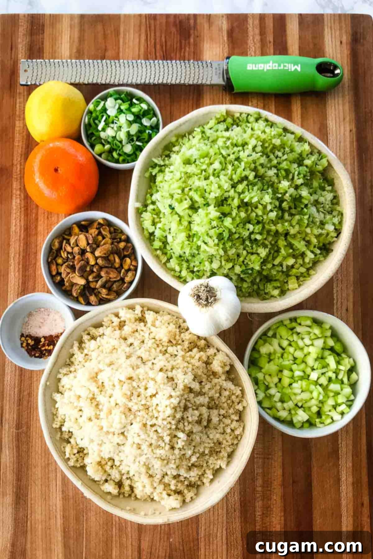 Ingredients laid out for a riced broccoli and quinoa salad, including an orange, lemon, chopped celery, pistachios, salt, and pepper, showcasing fresh, wholesome components.