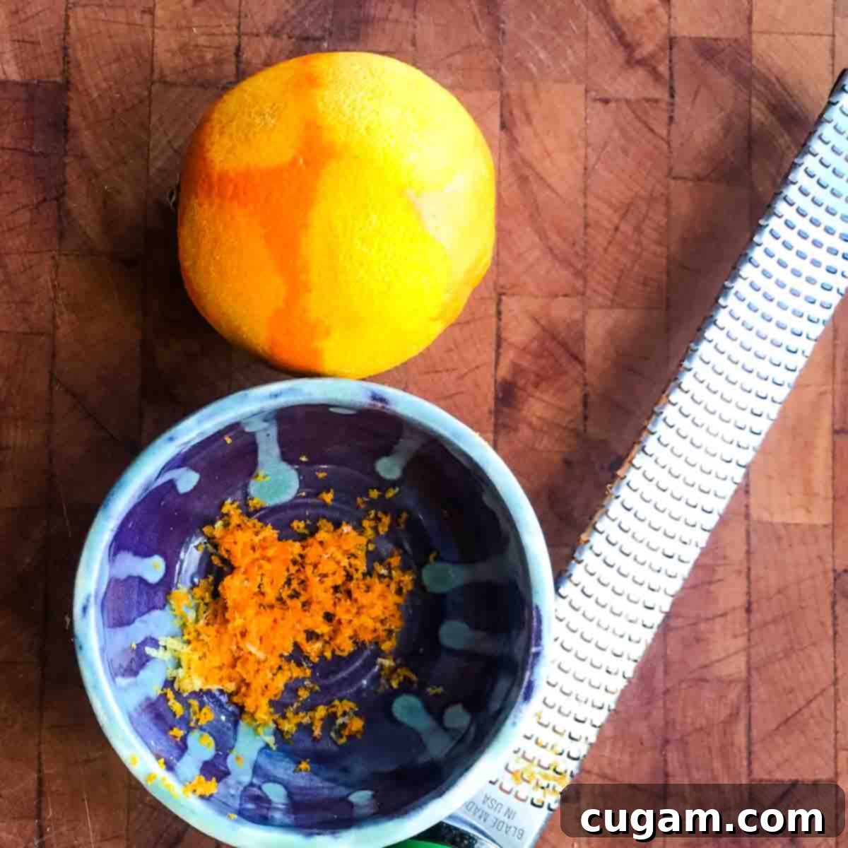 An orange being zested into a small bowl with a microplane, preparing the fresh citrus dressing ingredients.