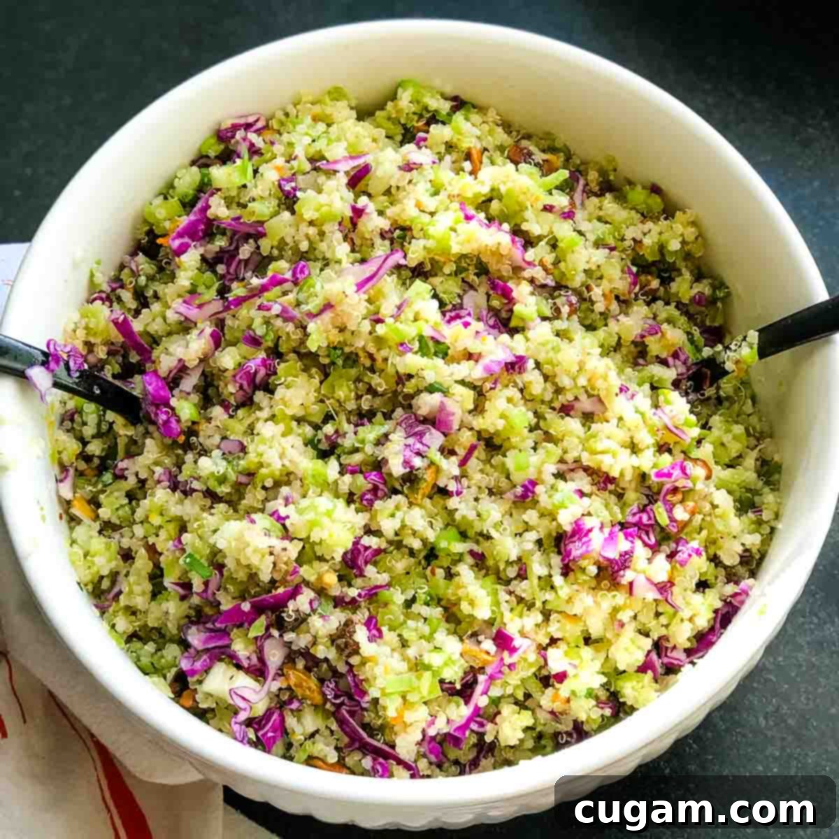 A large bowl filled with riced broccoli, quinoa, red cabbage, pistachios, and scallions, ready for the final dressing and toss.