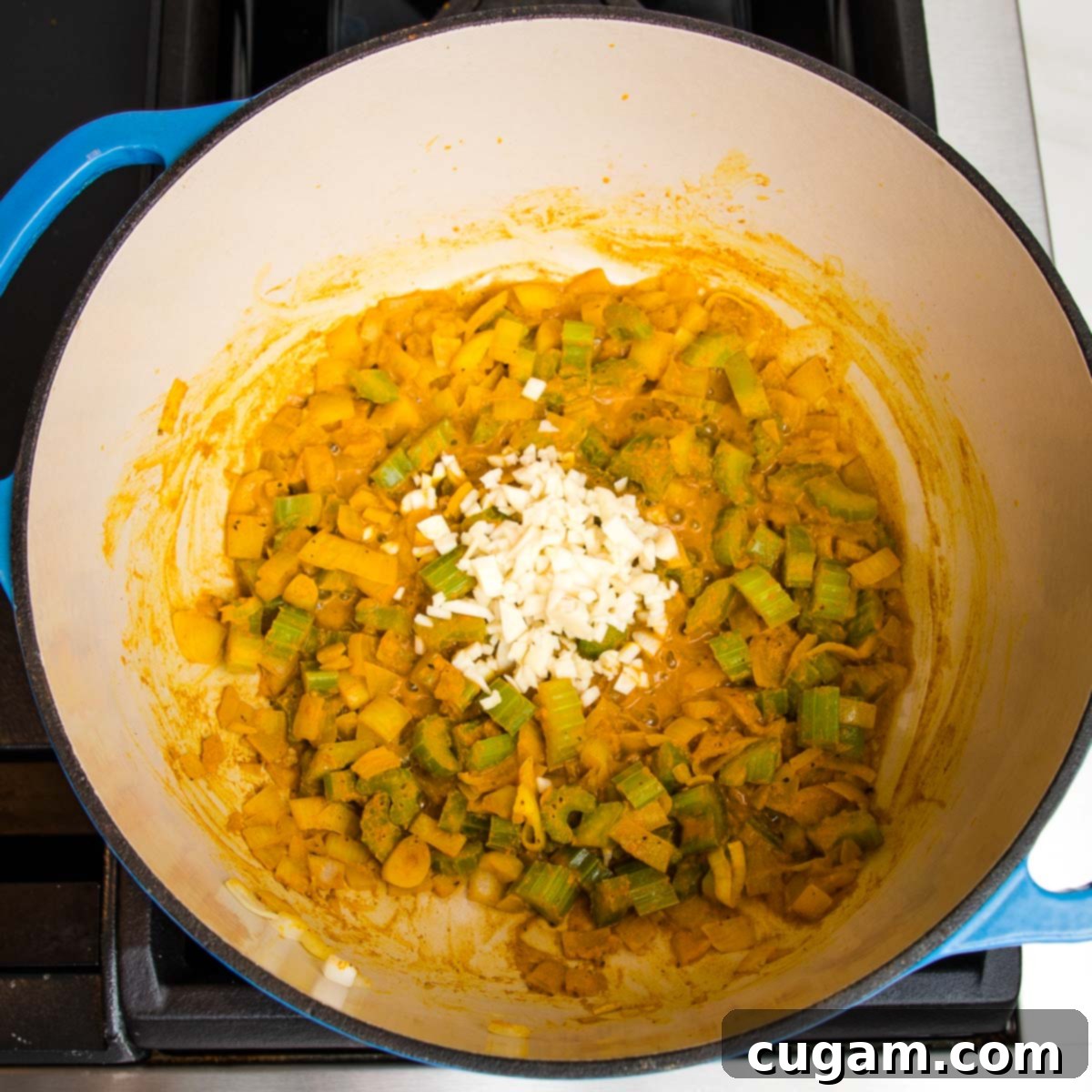 A close-up of a Dutch oven where fragrant garlic has been stirred into the turmeric-sautéed onions and celery, creating a rich aromatic base for the pureed parsnip and kale soup.
