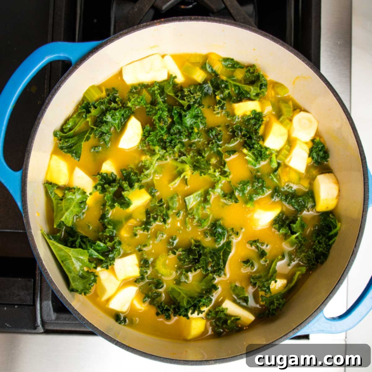 A Dutch oven on the stove, filled with a rich, yellowish-orange broth, cubes of parsnips, and abundant kale, brought to a boil before simmering to create a flavorful soup base.