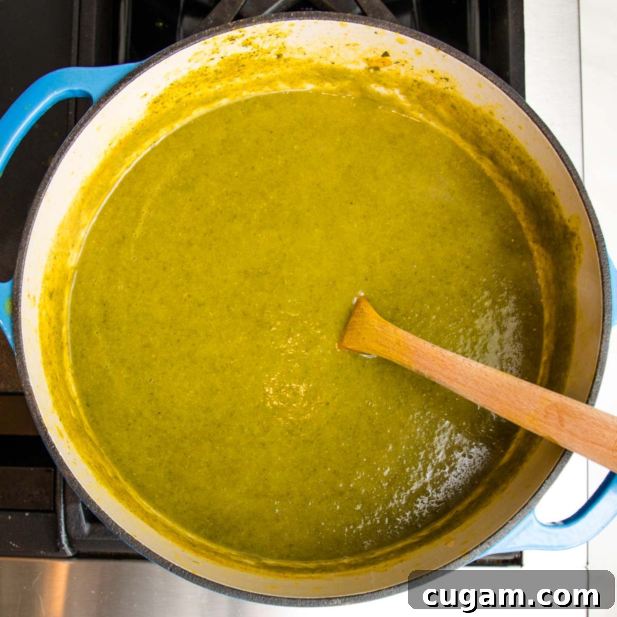 A blue Dutch oven on the stovetop, filled with a smooth, pureed green kale and parsnip soup, with a wooden spoon resting inside, indicating a ready-to-serve healthy vegan meal.