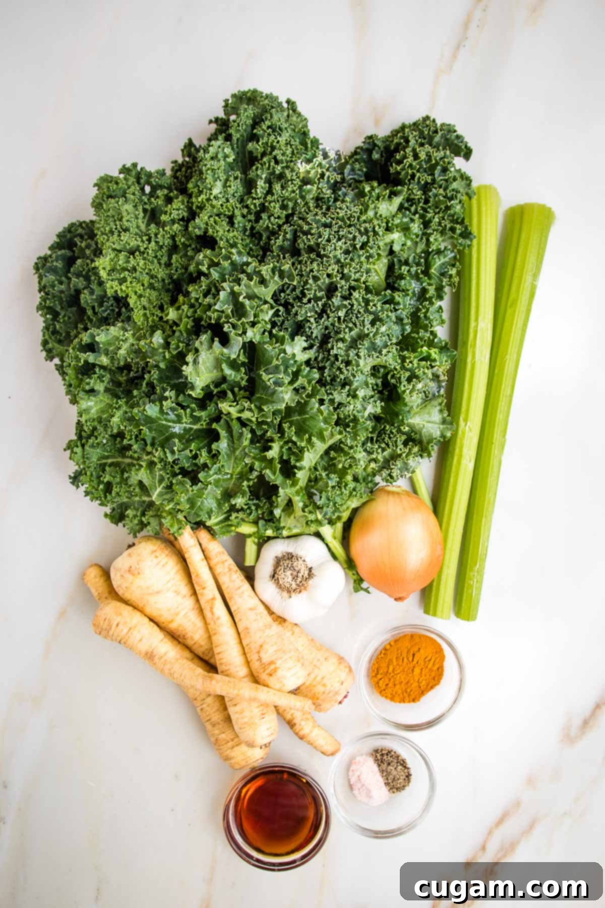 A colorful array of raw ingredients for a healthy pureed vegetable soup, including fresh curly kale, crisp celery stalks, sweet parsnips, pungent onion and garlic, earthy turmeric, salt, pepper, and a bottle of maple syrup, laid out on a wooden surface.