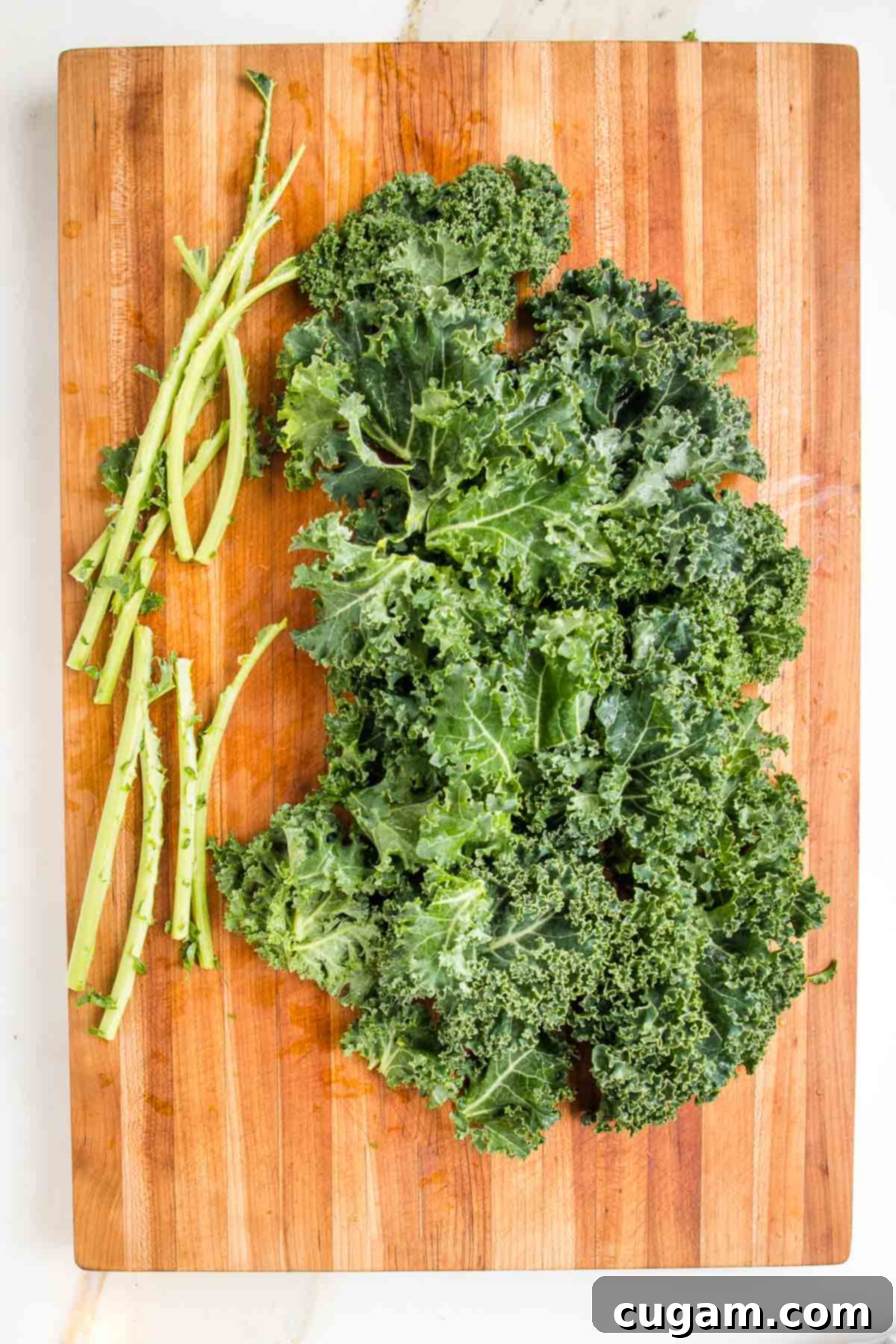 A rustic wooden board showcasing fresh curly kale with its woody stems carefully removed and placed to the side, ready for tearing into smaller pieces for soup.
