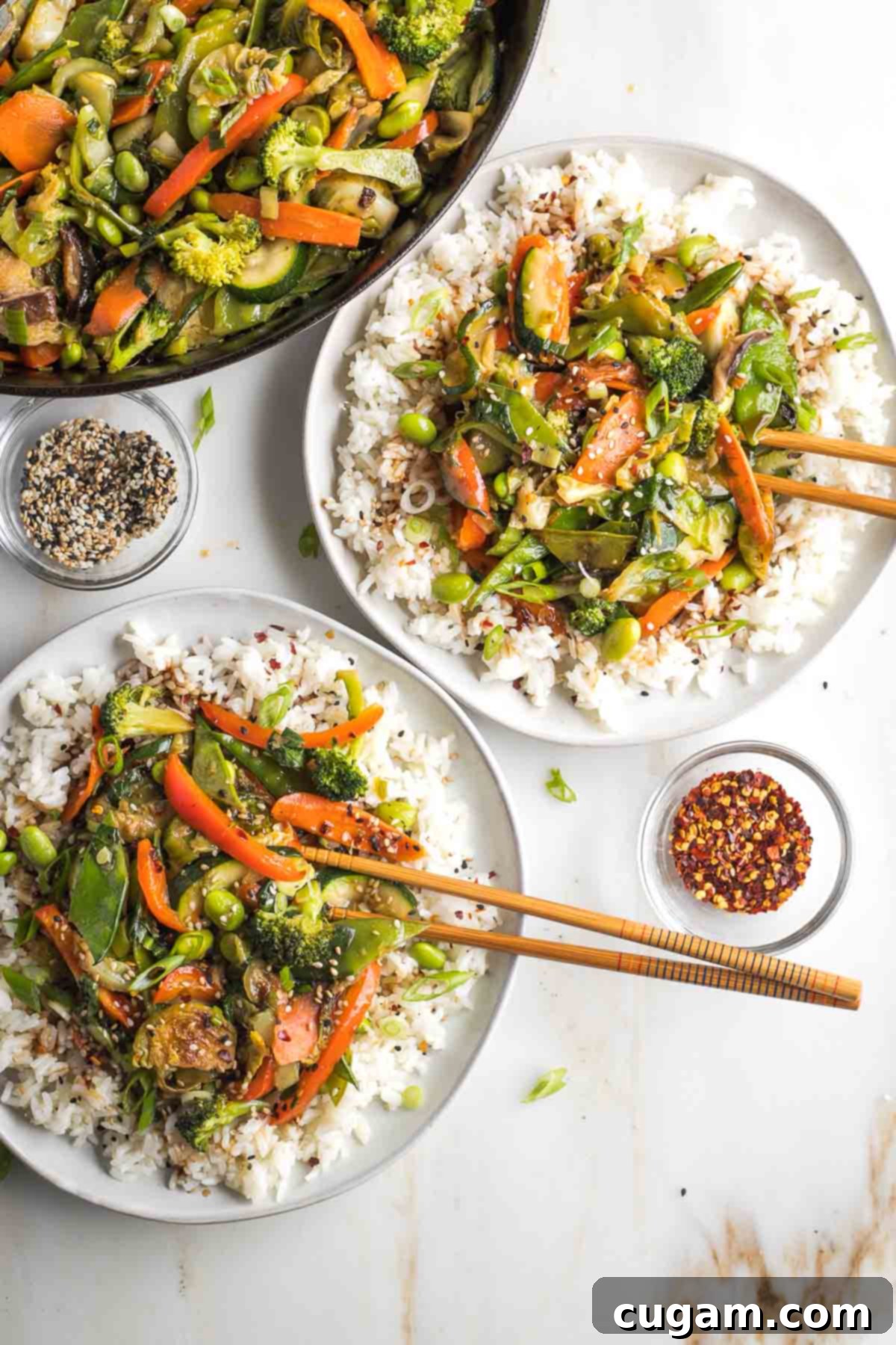 Two plates of rice topped with stir-fried vegetables with teriyaki sauce, garnished with sesame seeds.