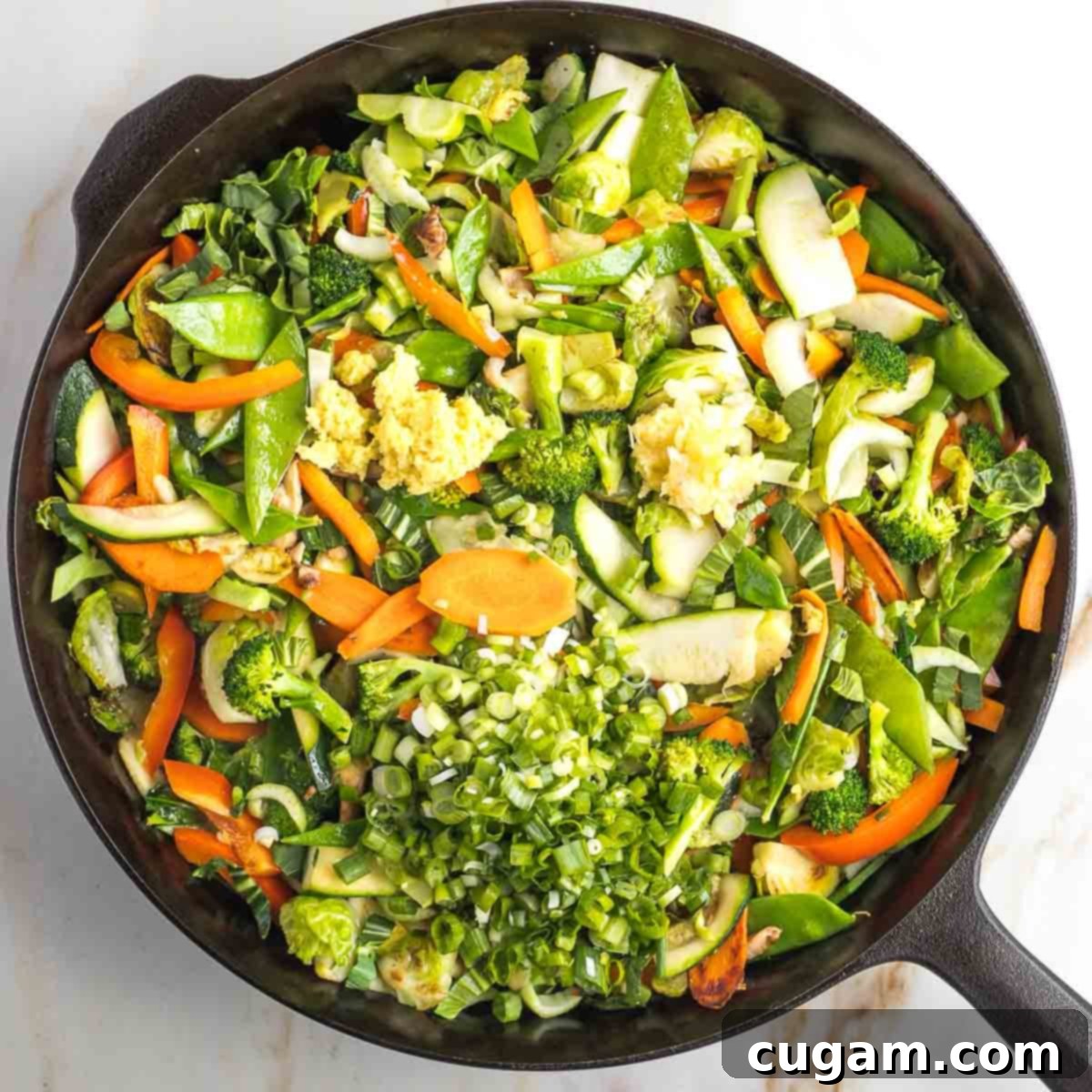 Garlic, ginger, and scallions, along with the remaining sesame oil, being added to the stir-fried vegetables.