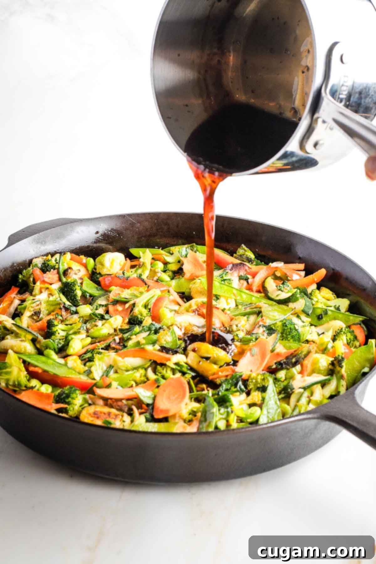 Reheated teriyaki sauce being poured over the finished stir-fried vegetables in the pan.