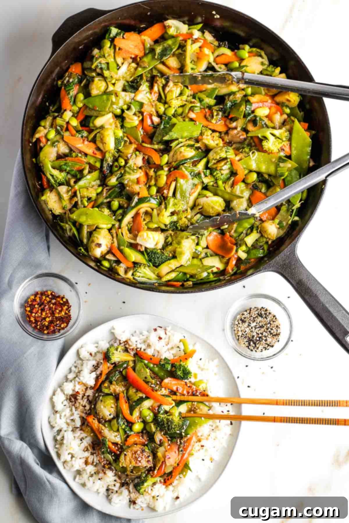 Large pan of stir fry veggies, plus a plate of rice topped with the vegetables, garnished with sesame seeds.