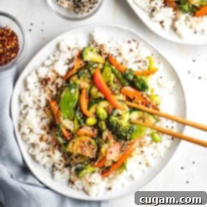 Plate of rice covered with vegetables and teriyaki sauce, sprinkled with sesame seeds.