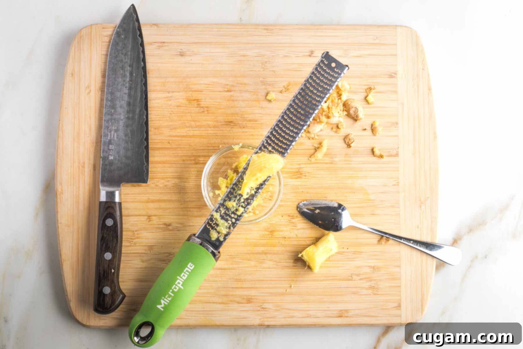 Grapefruit spoon peeling skin off fresh ginger and microplane grating it into a bowl.