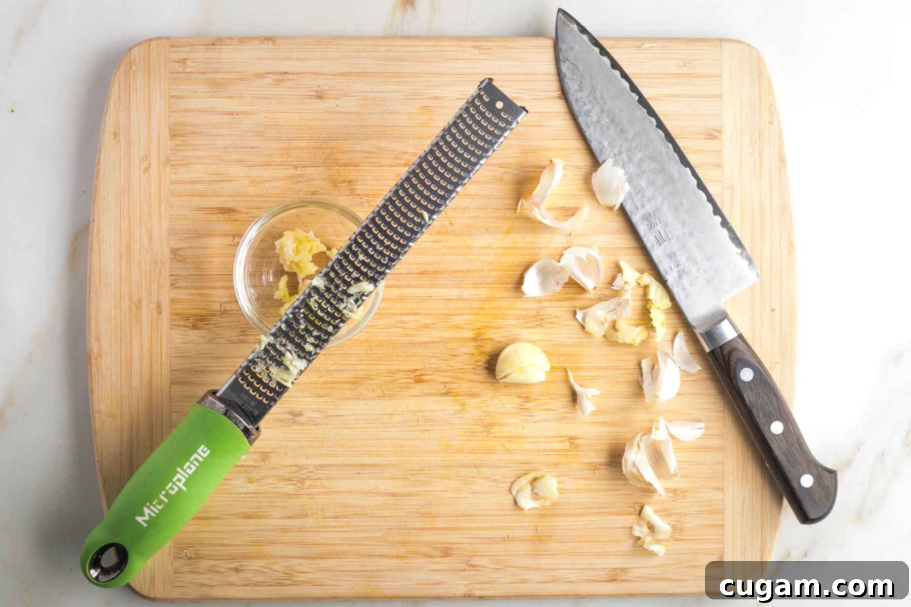 Peeled cloves of garlic being grated into a dish on a microplane.