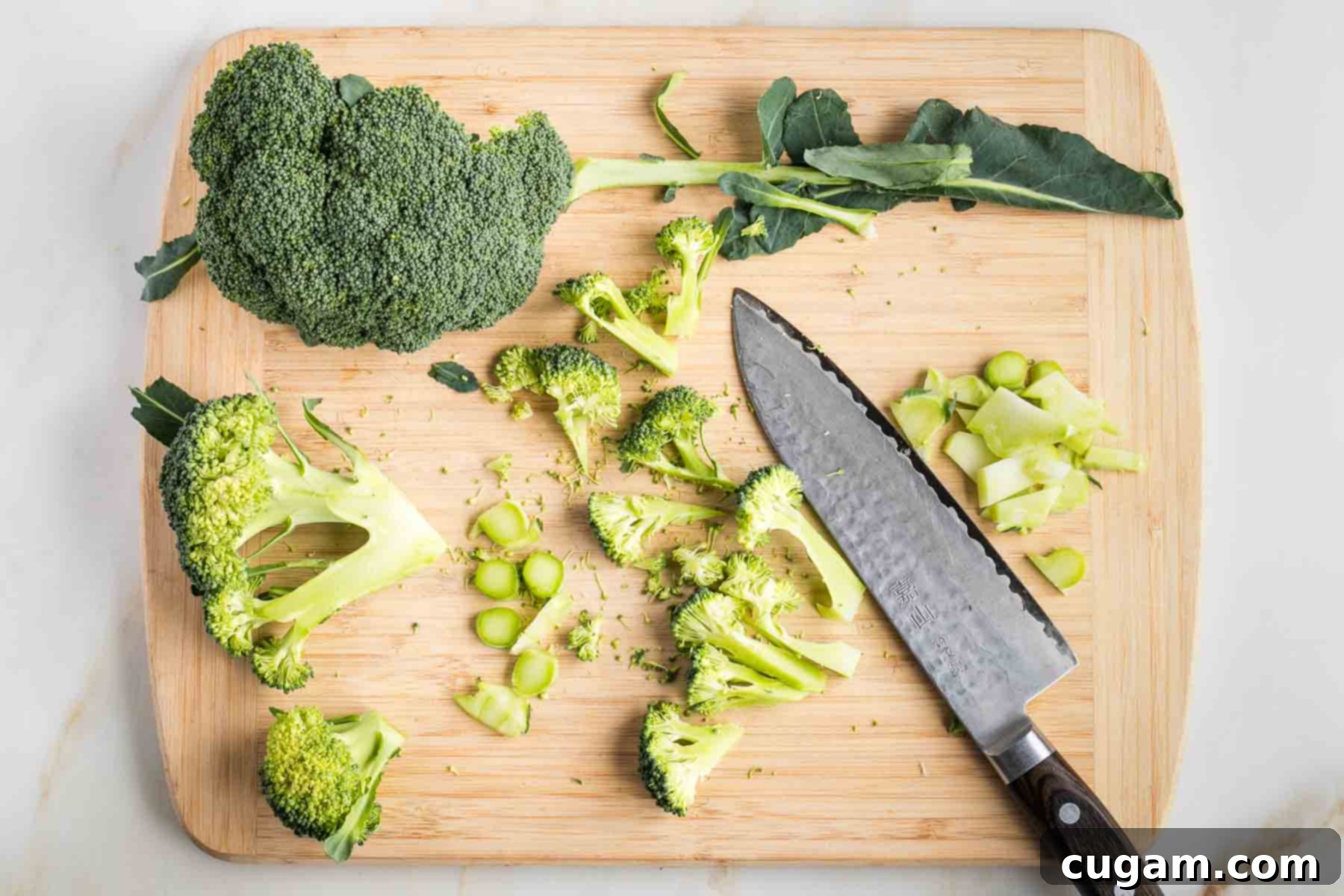 Chef's knife cutting broccoli stems into discs and crowns into florets.