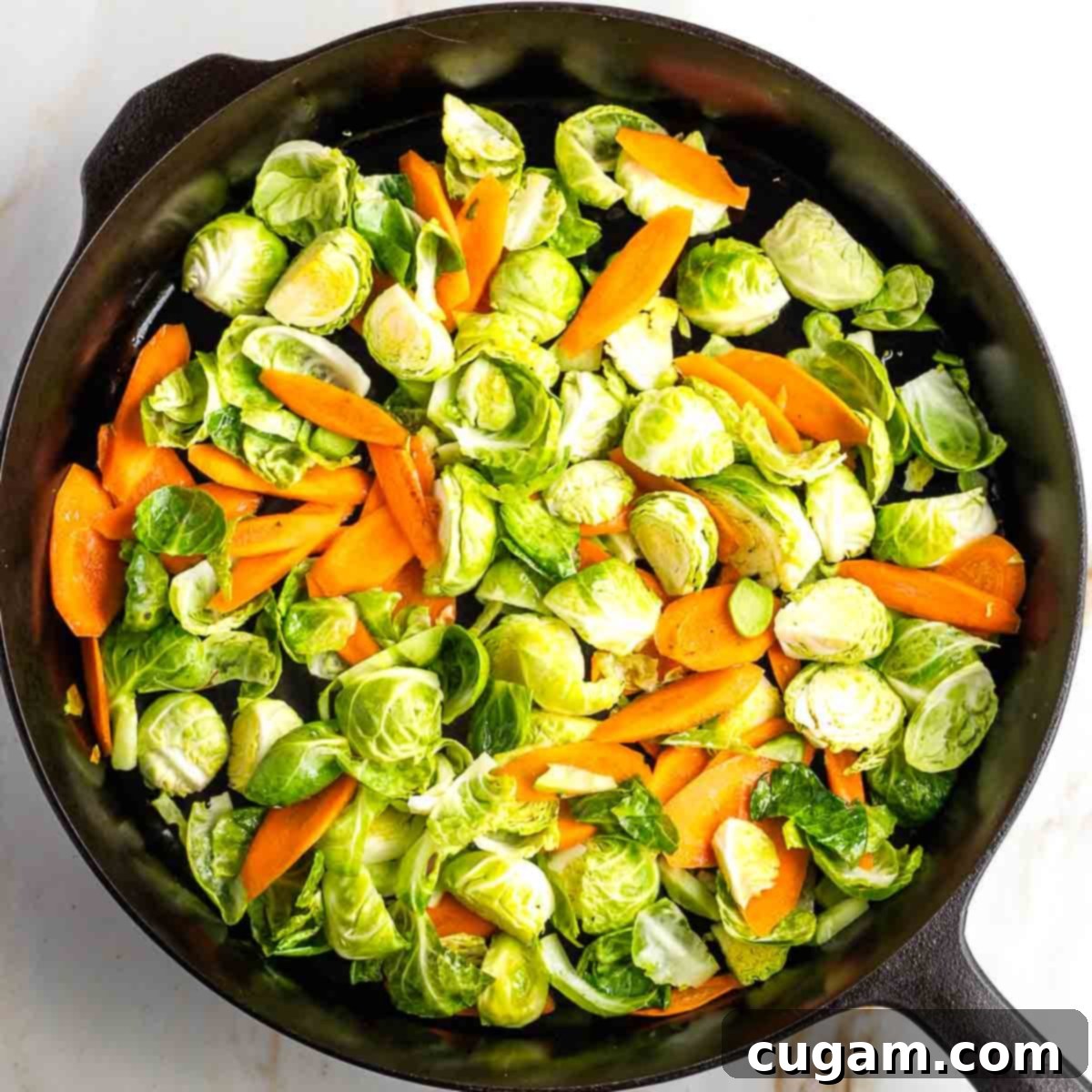 Harder vegetables (carrots, Brussels sprouts, broccoli stems) being stir-fried in a large wok with sesame oil.