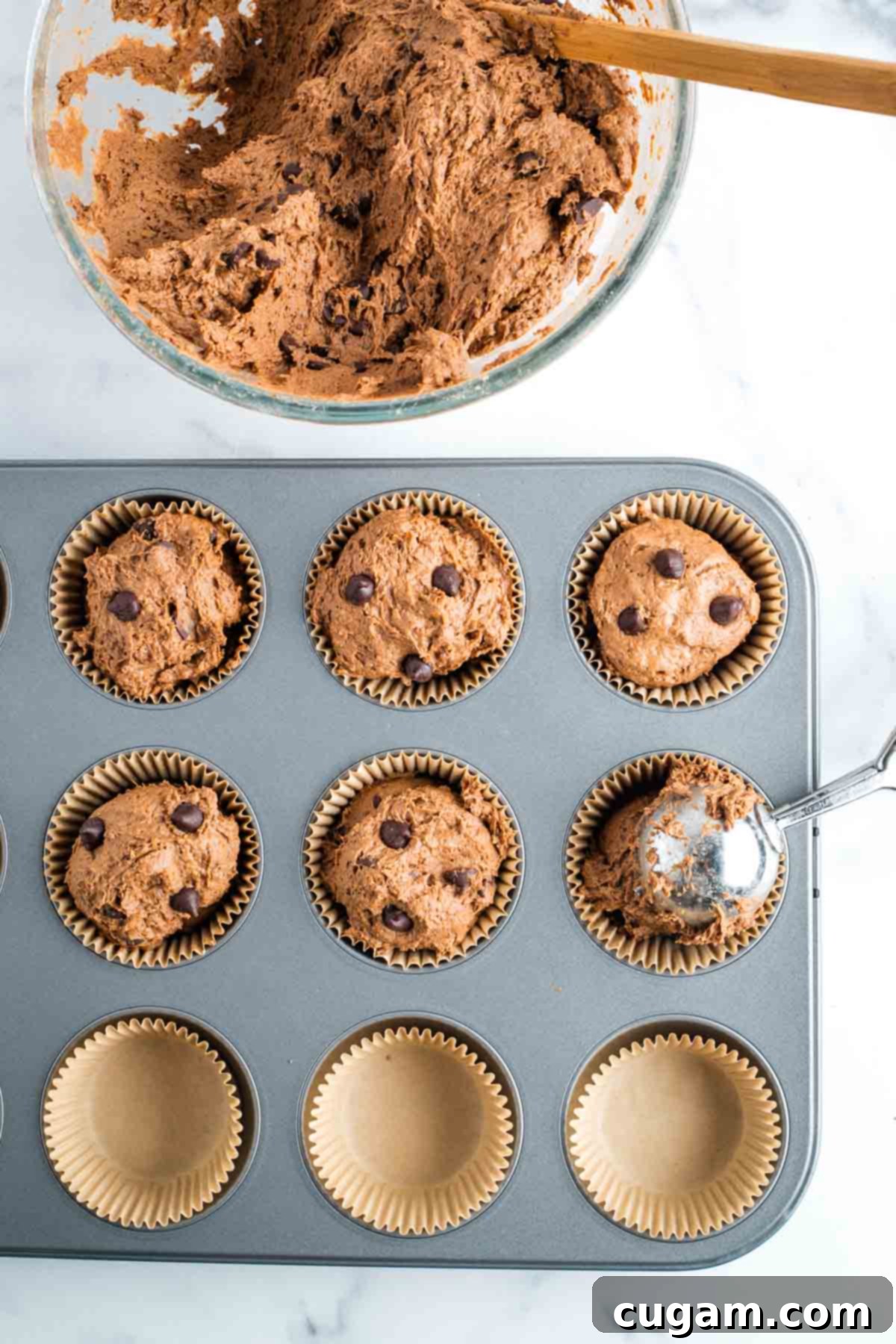 Scooping chocolate chocolate chip muffin batter into parchment lined muffin tins.