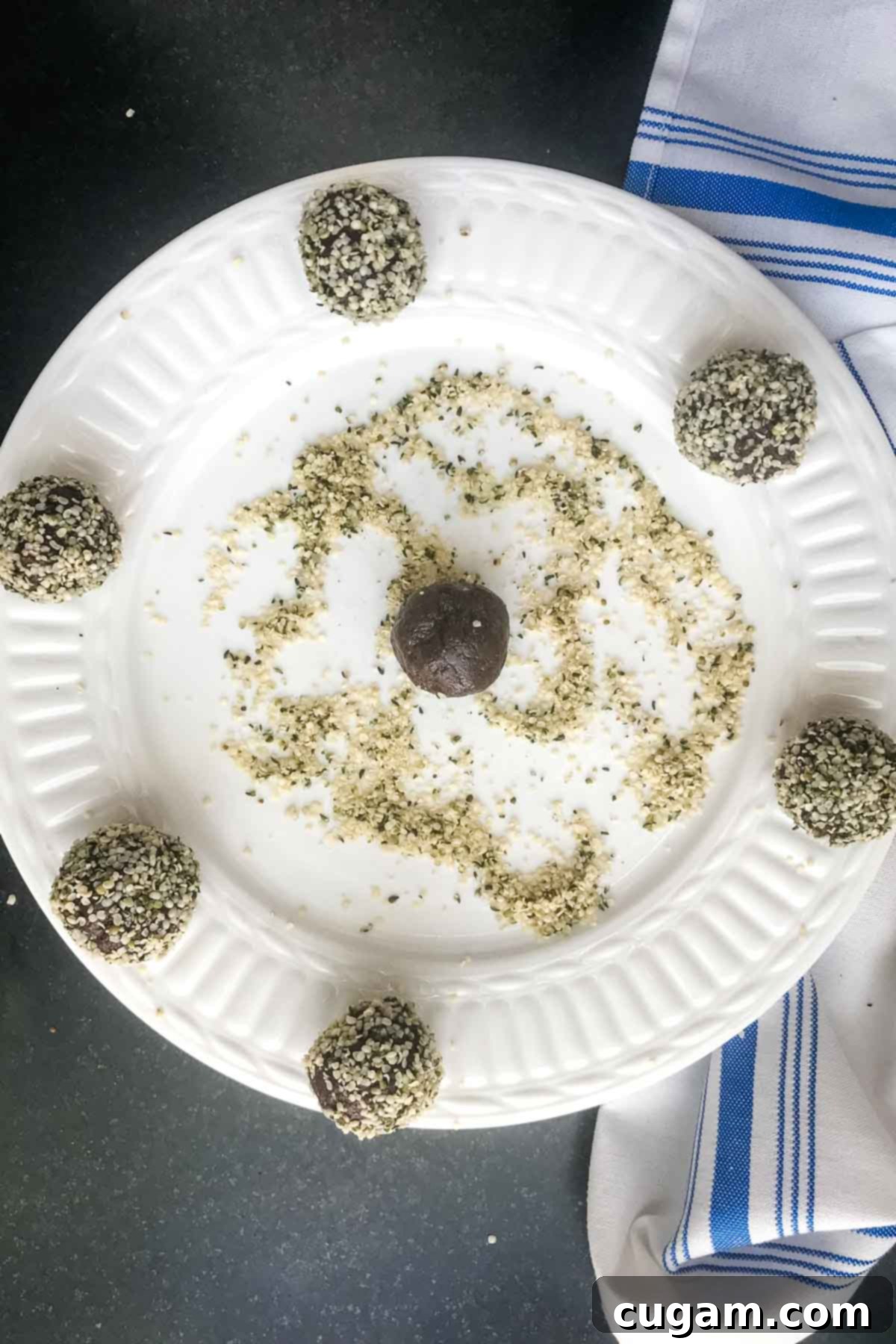 Rolling chocolate balls into hemp seeds and placing them on the outer rim of a white plate.