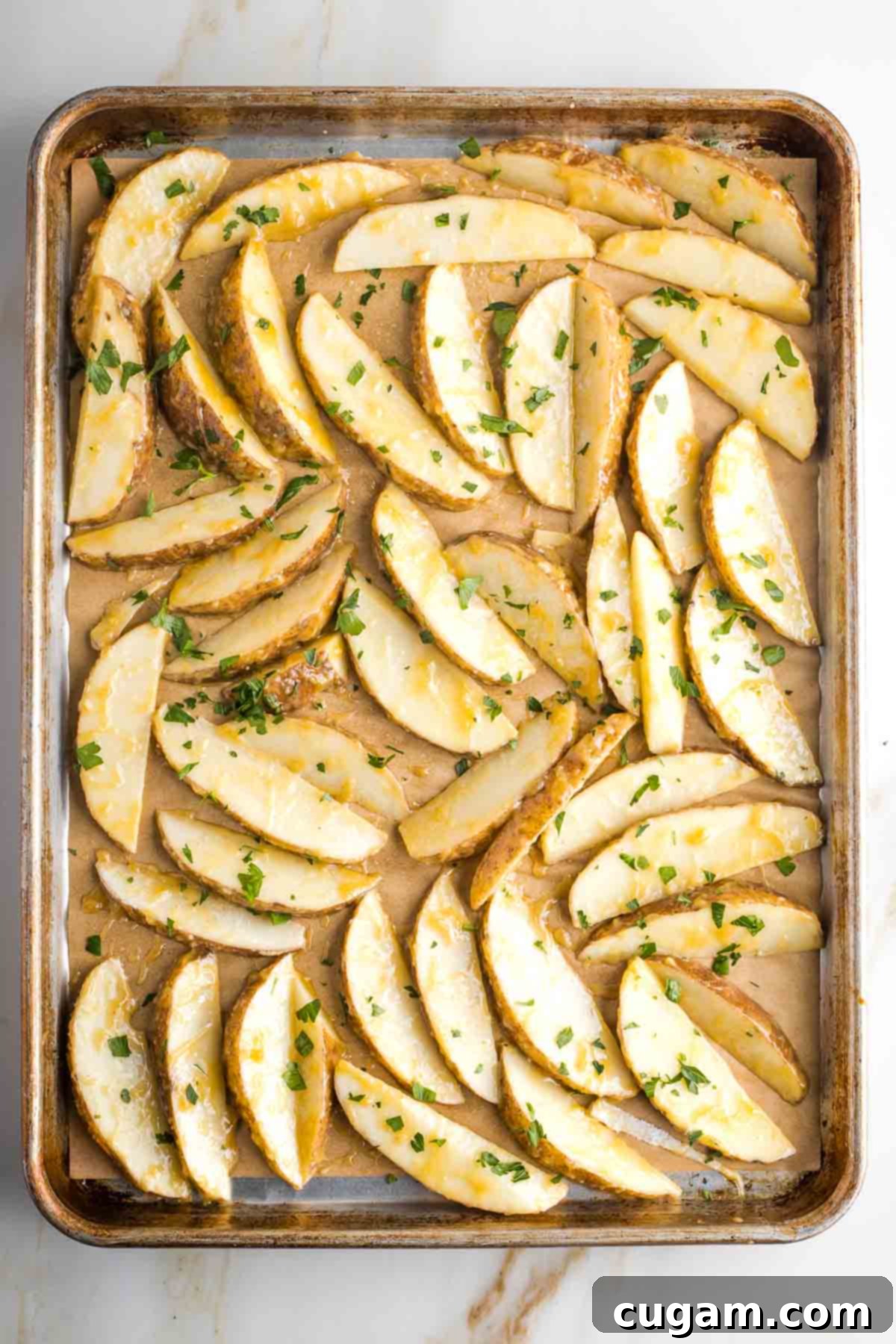 Potato wedges with miso marinade and parsley in a single layer on a baking tray.