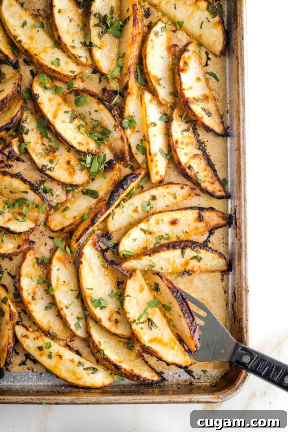 Spatula serving crispy potato wedges right off the baking pan.