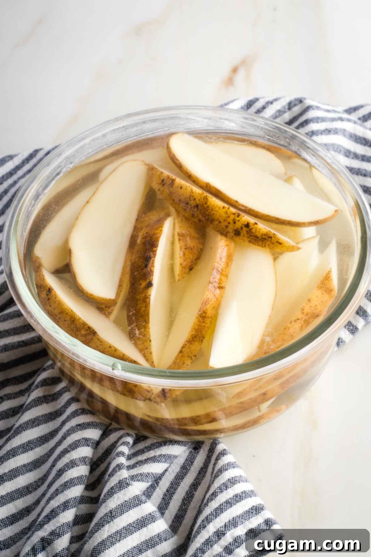 Large glass bowl filled with water, soaking potato wedges.