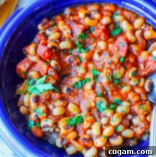 close up photo of beans with sausage and tomatoes on a blue plate with spoon, horizontal