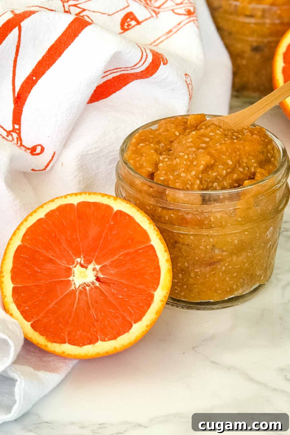 Small jar orange chia seed marmalade plus half an orange with bright orange inside showing.