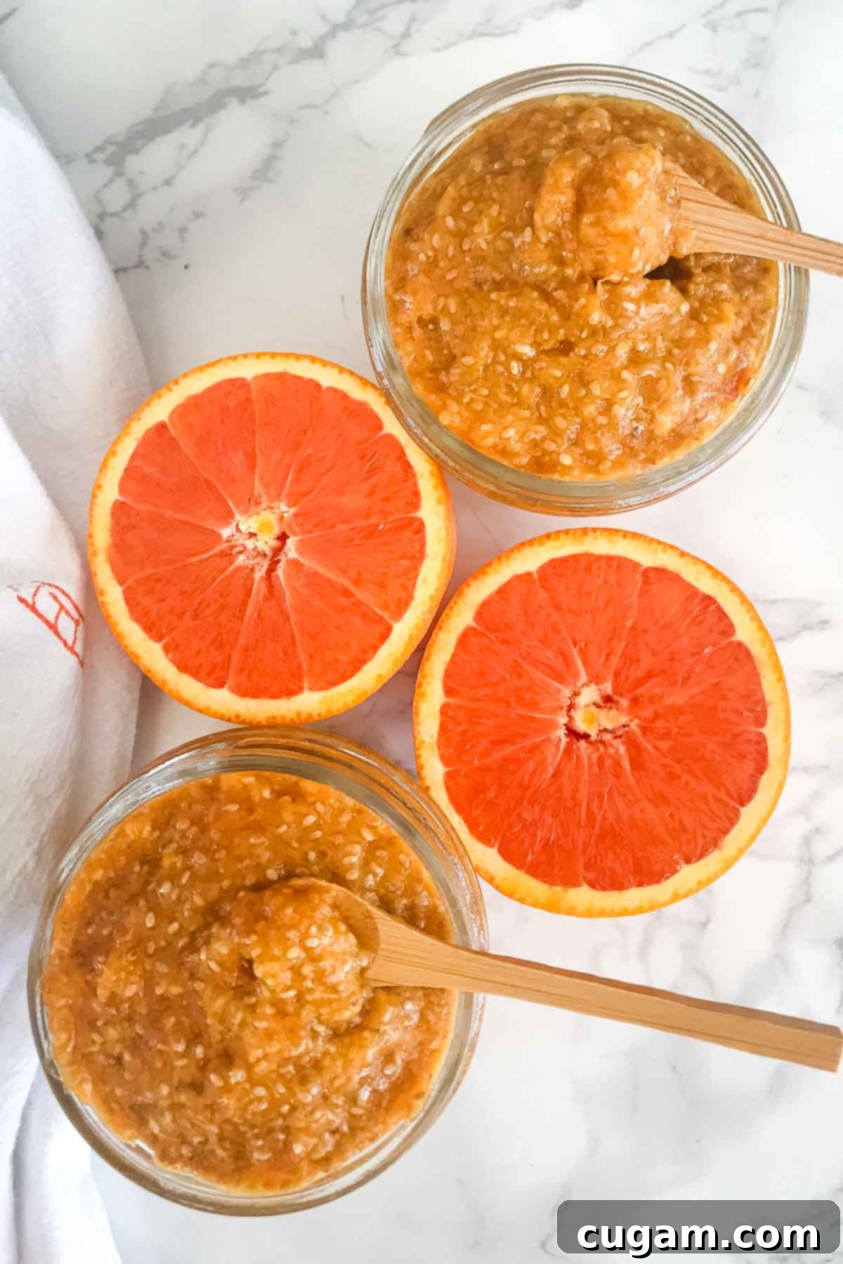 Small mason jars filled with orange chia marmalade and an orange cut in half, showing the bright flesh.