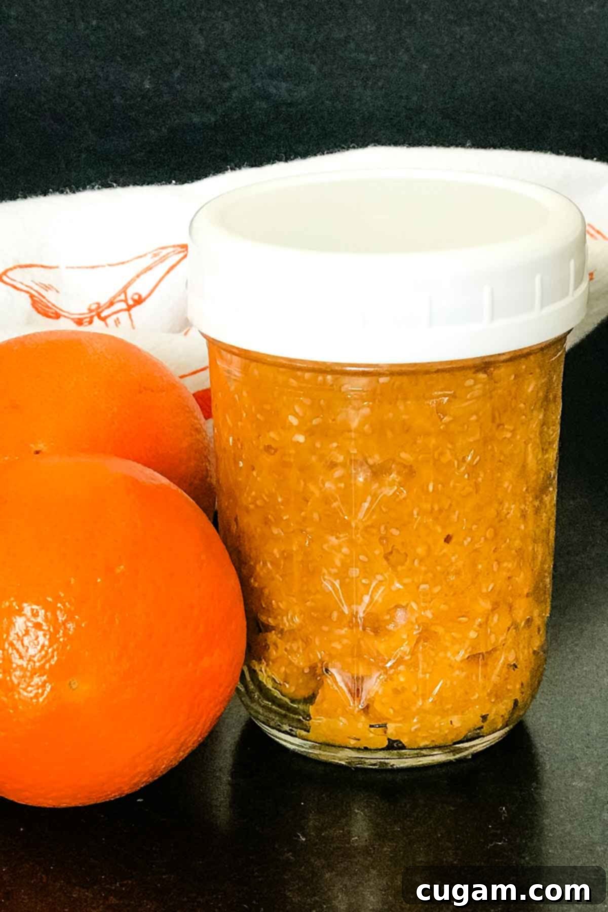 Mason jar filled with orange marmalade, surrounded by fresh oranges.