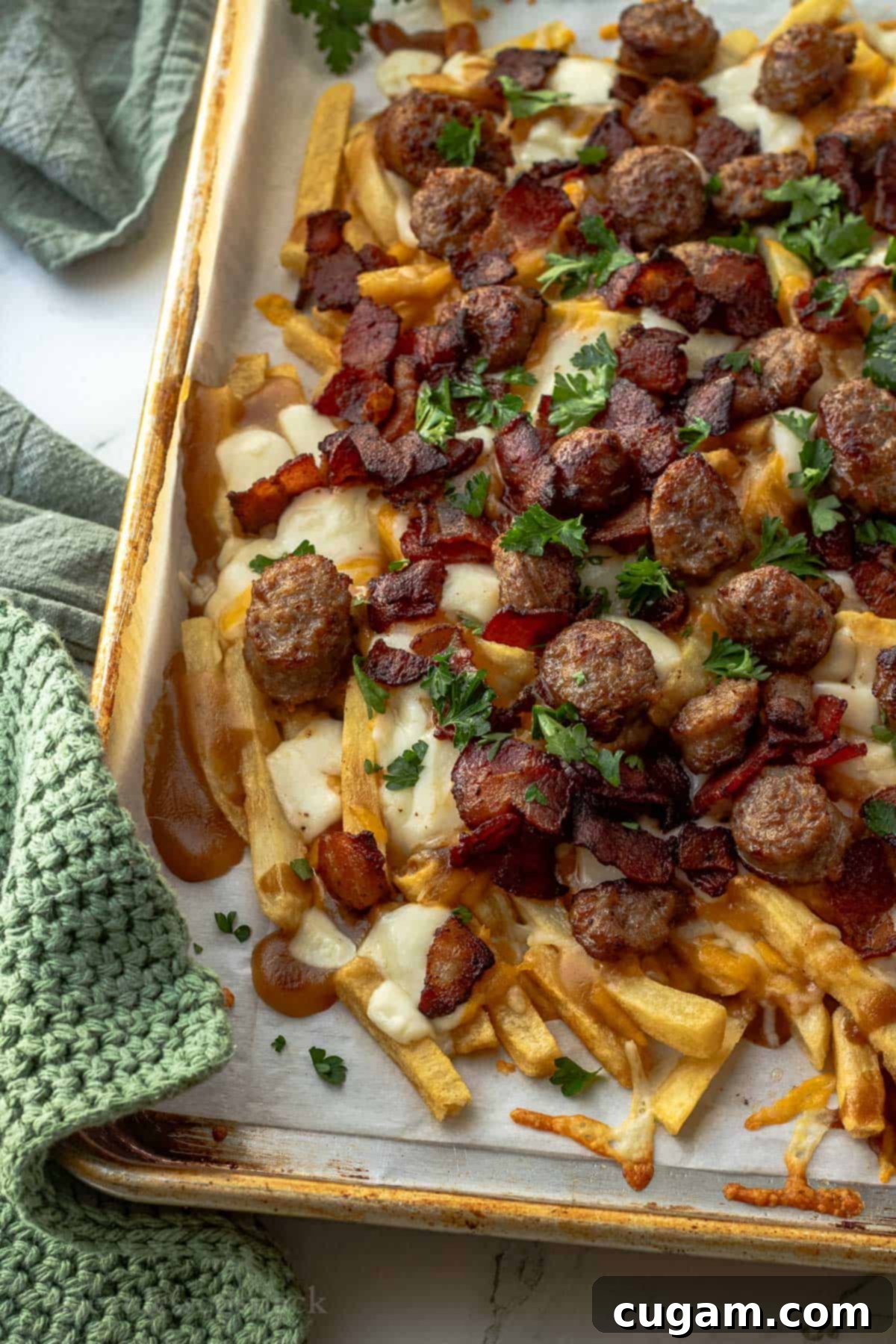 Metal pan with baked french fries, cheese, sausage, and bacon over parchment paper.