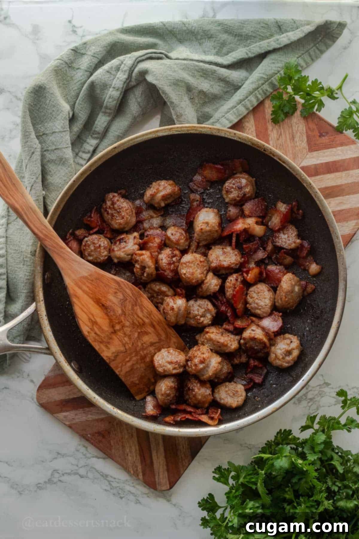 Metal pan with cooked sausage and bacon with wood spatula.