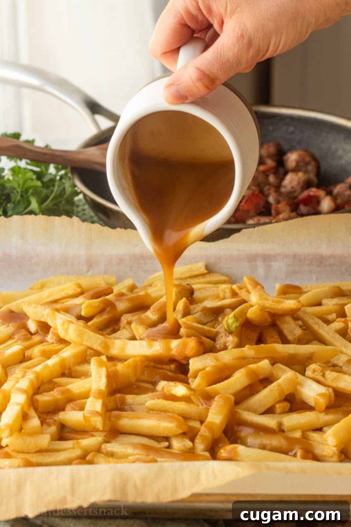 Pouring gravy over baked french fries on metal pan.
