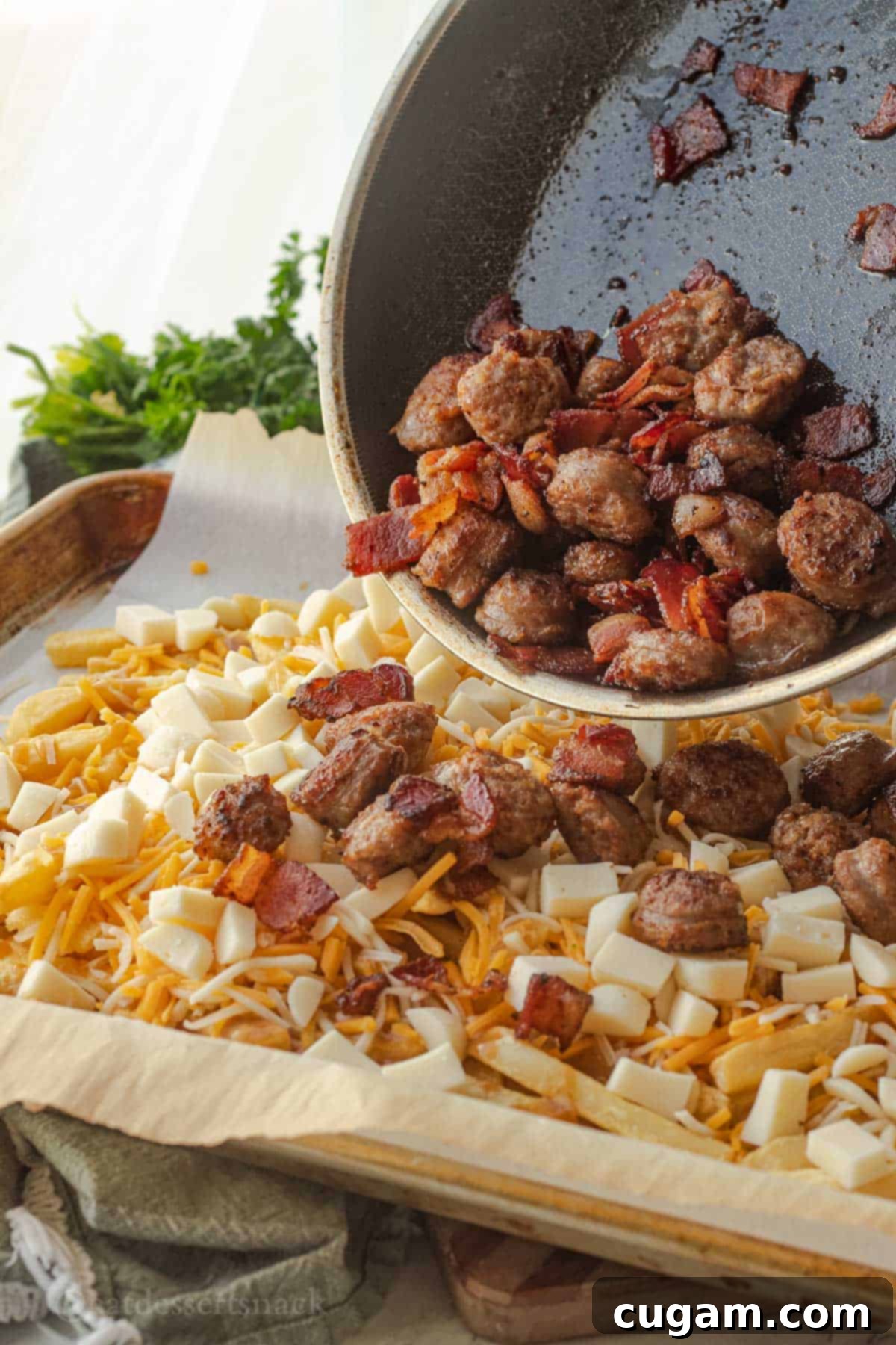 Pouring cooked sausage and bacon over pan of fries with cheese.