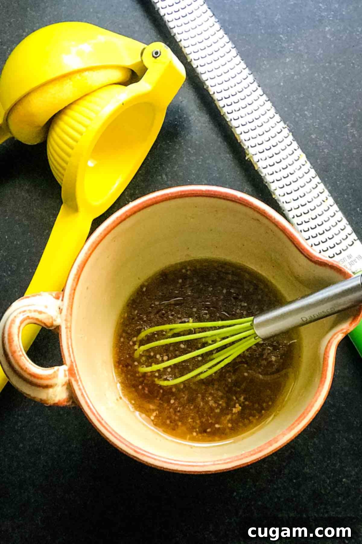Small pitcher mixing up a vinaigrette with a microplane grater and a lemon squeezer on the side.