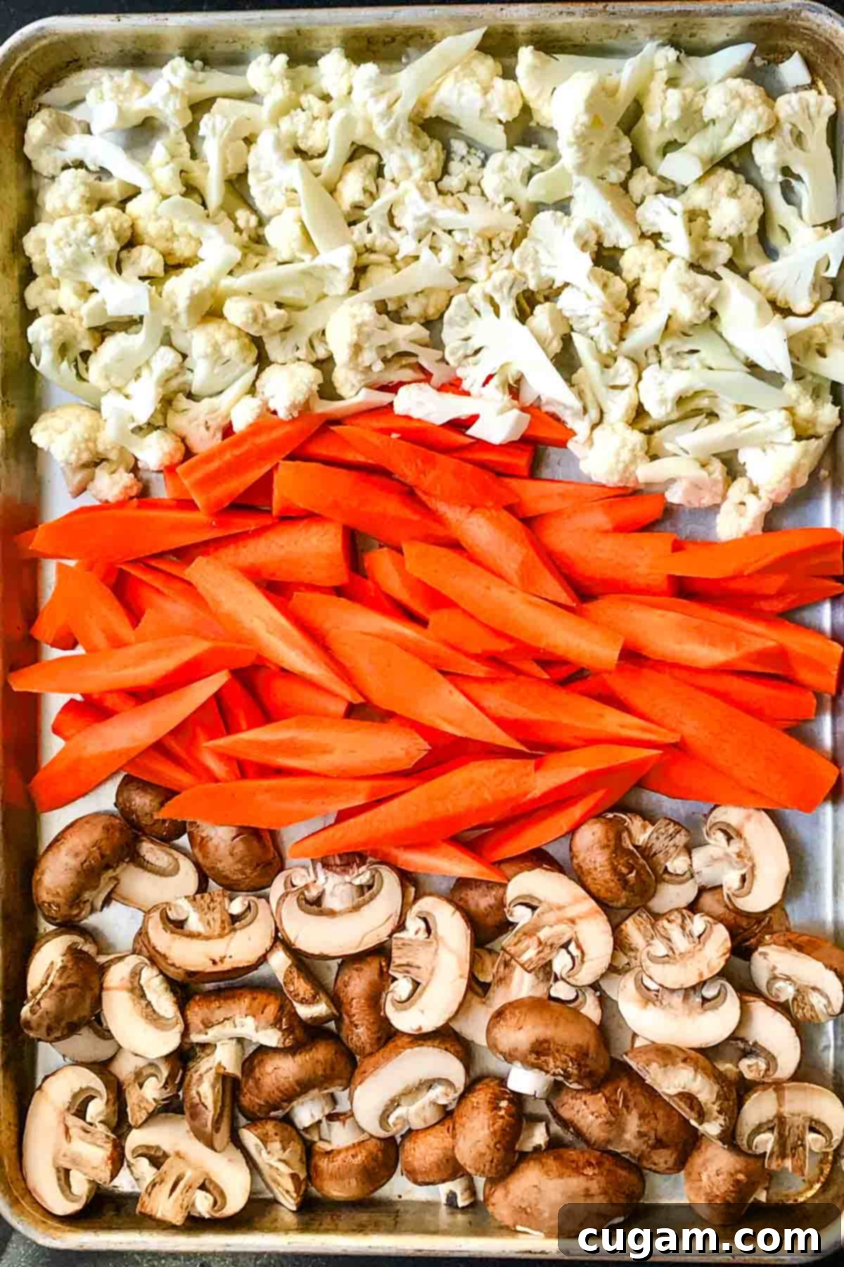 Rows of cauliflower florets, carrot spears and sliced mushrooms on a large timmed baking sheet.