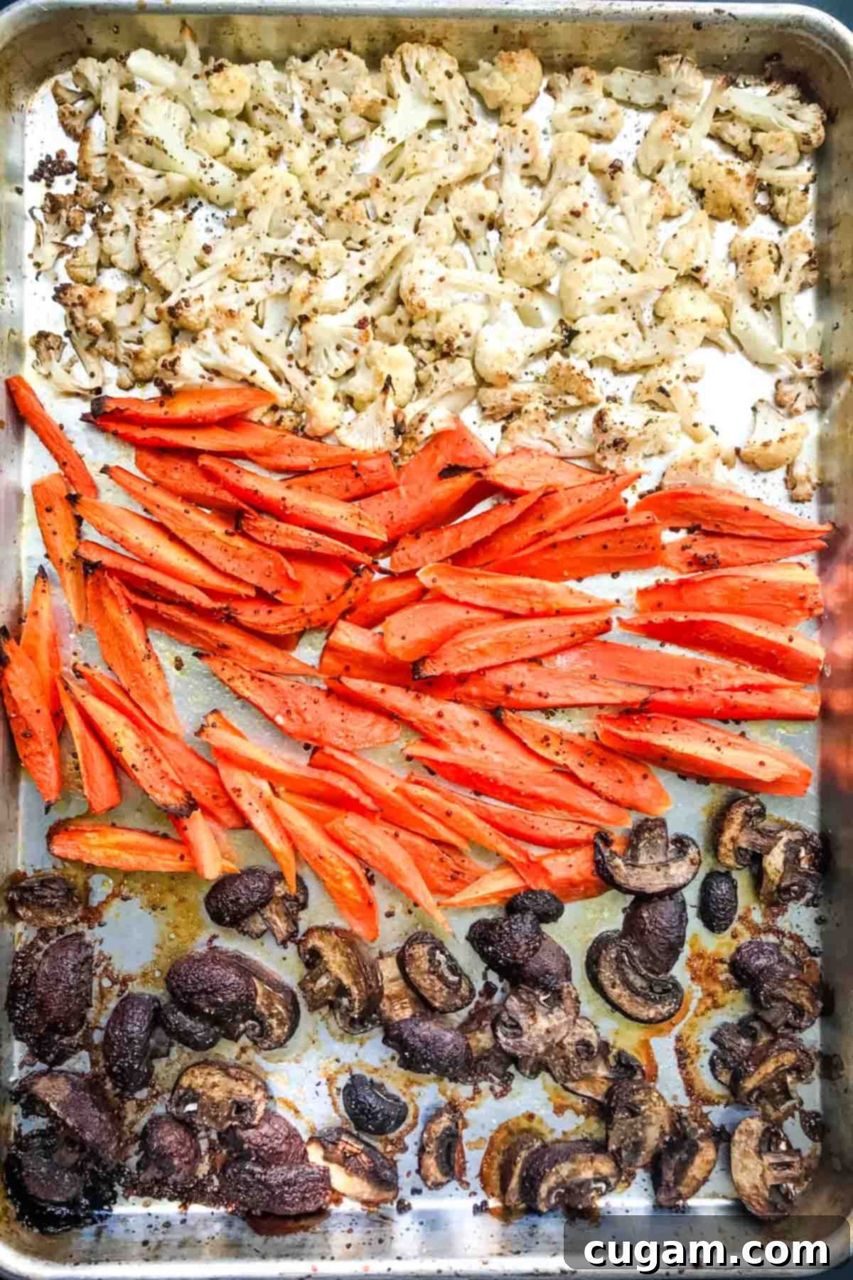 Roasted cauliflower florets, carrot spears and sliced mushrooms on a large rimmed baking tray.