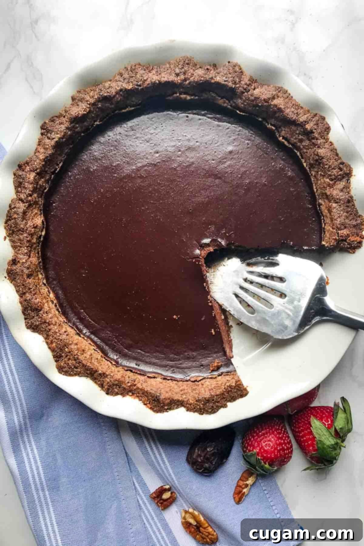Large slice missing from a chocolate pudding pie, surrounded by strawberries, dates and pecans.