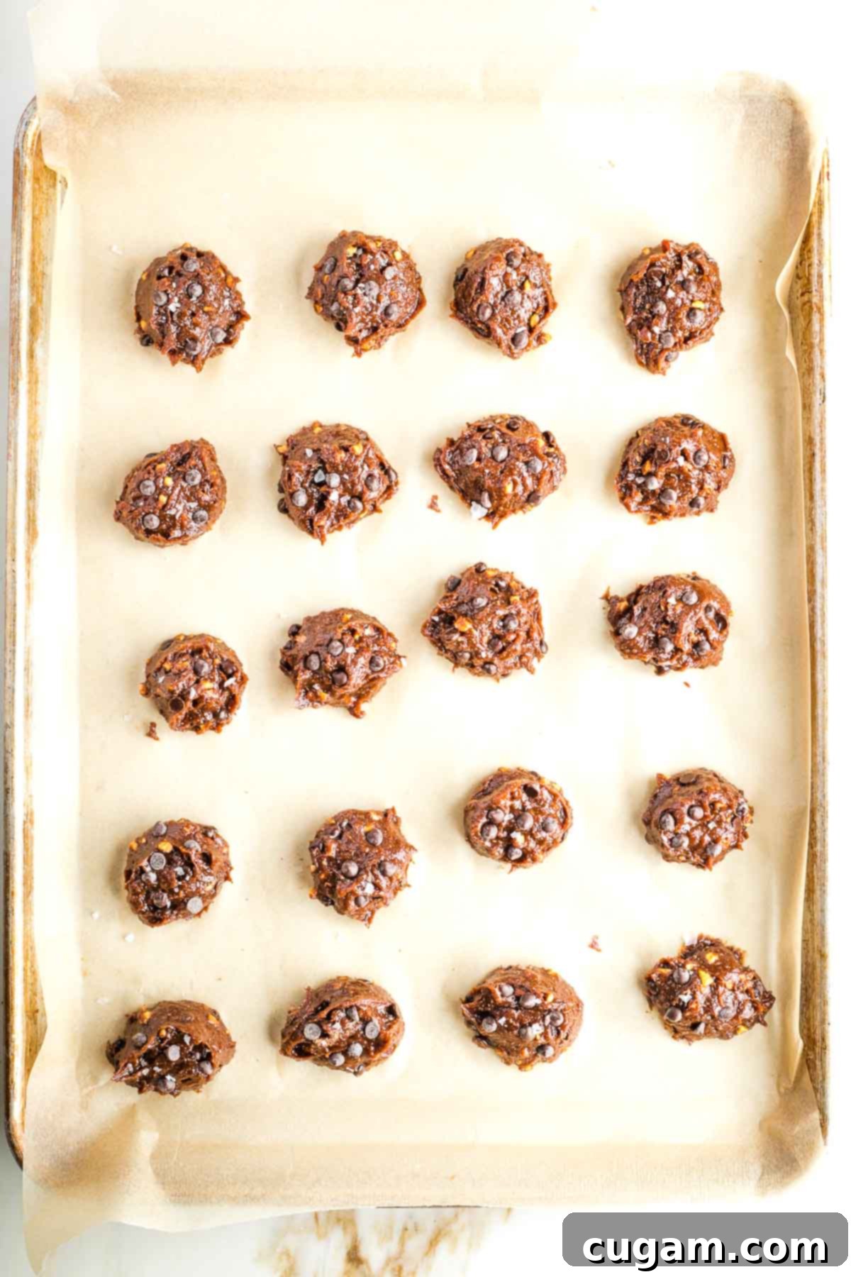 A baking tray filled with perfectly scooped double chocolate chip cookie dough, adorned with extra chocolate chips on top.