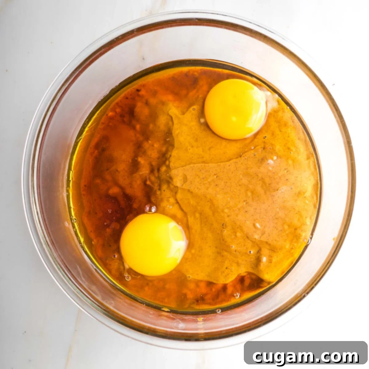 Wet ingredients (almond butter, maple syrup, and eggs) being mixed in a glass bowl with a spatula.