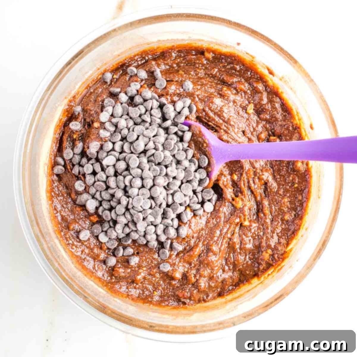 A bowl of rich chocolate cookie dough, with a generous handful of dark chocolate chips sprinkled on top, ready to be folded in.