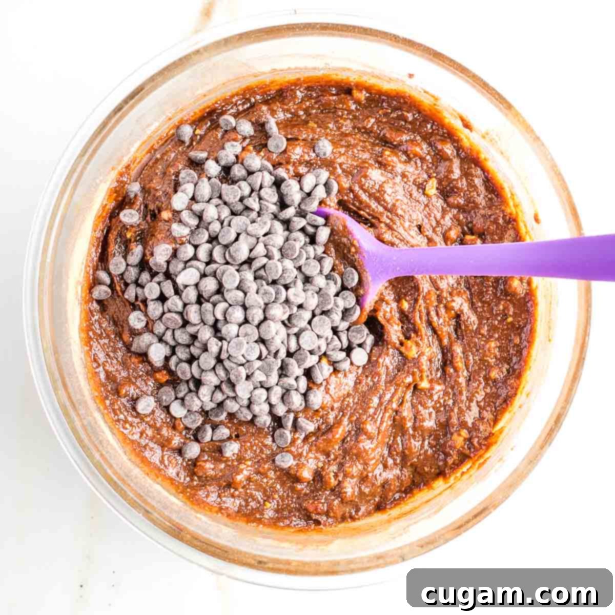 A handful of dark chocolate chips resting on top of a bowl of fully mixed, rich chocolate cookie dough, ready to be folded in.