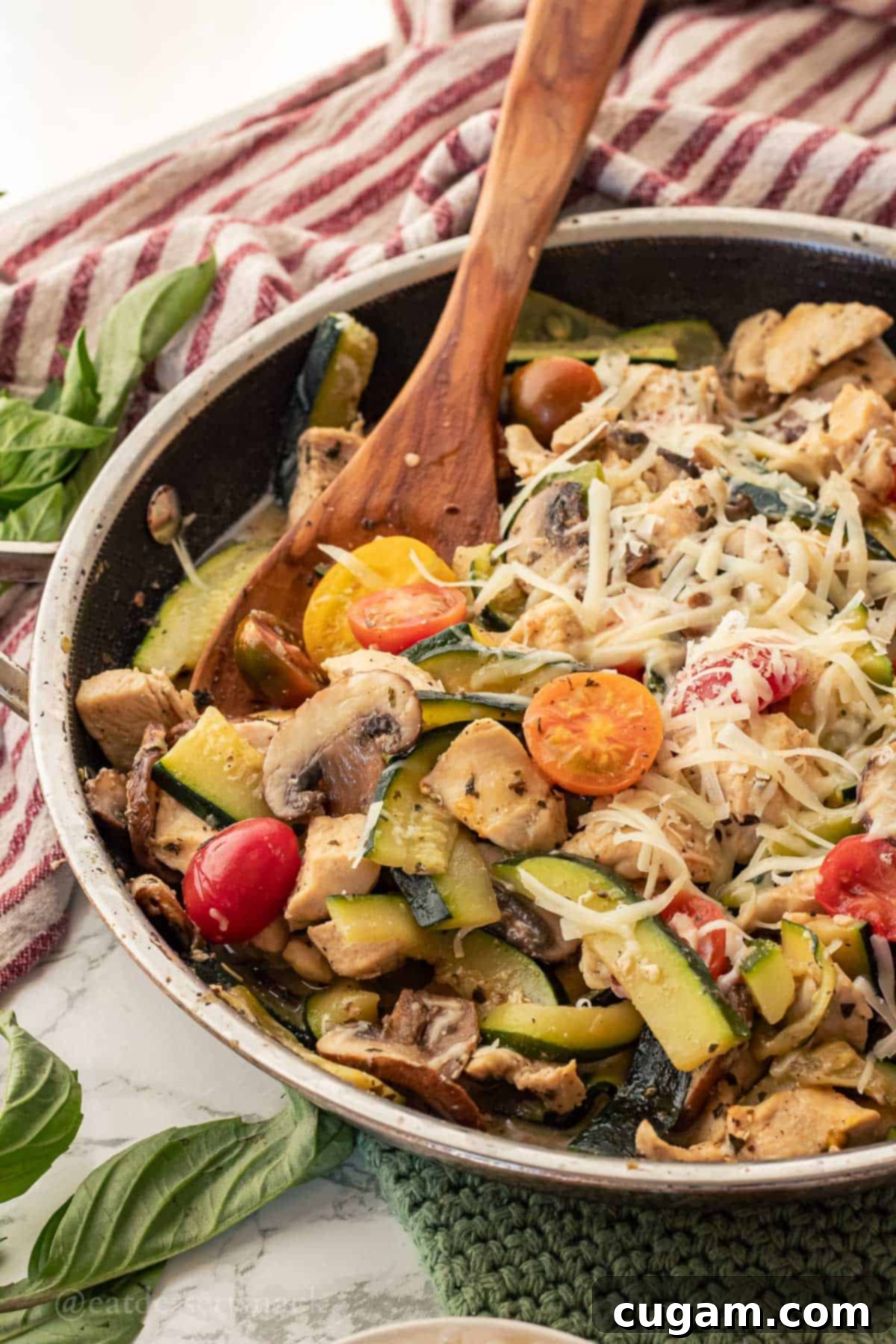 Savory Chicken Zucchini Tomato Skillet 2 Close-up of a cooked Italian Chicken Zucchini Mushroom Skillet, garnished with fresh basil, tomatoes, and Parmesan cheese, served in a metal pan with a wooden spoon.