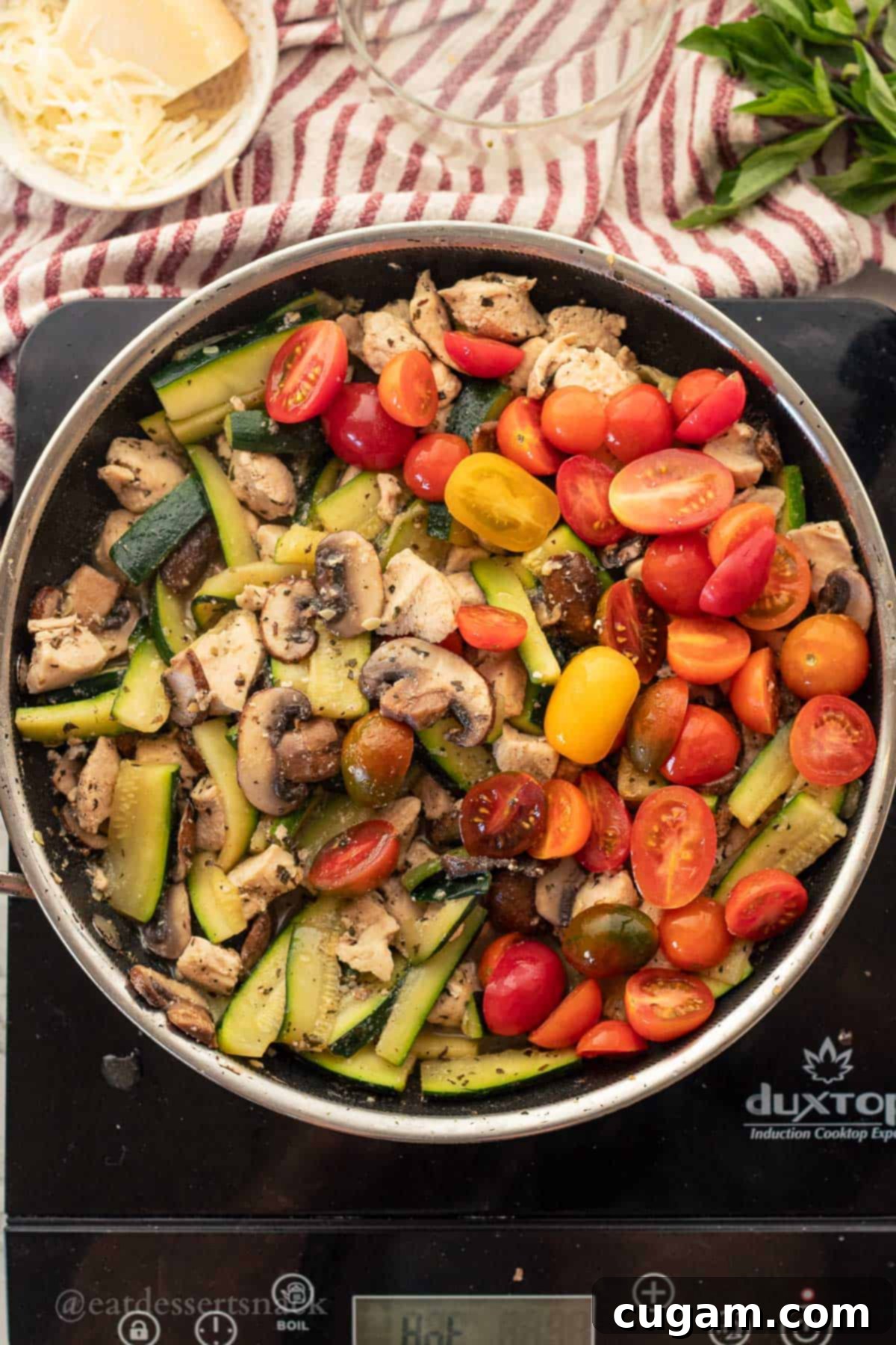 Savory Chicken Zucchini Tomato Skillet 6 Cooked chicken, zucchini, and mushrooms in a metal pan, with fresh grape tomatoes recently added and stirring to combine before the Italian dressing.