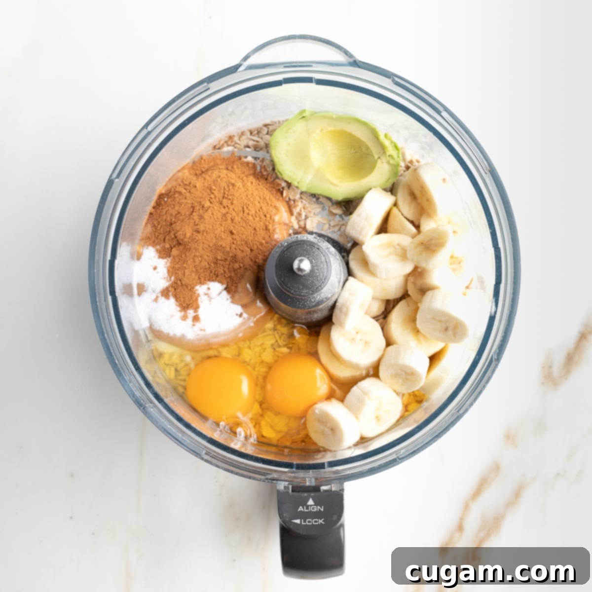 Bowl of food processor filled with eggs, cinnamon, banana slices, avocado and more hidden underneath, ready for blending.