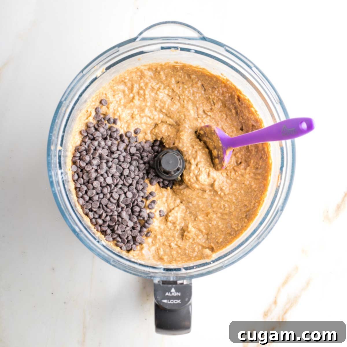 Banana oat muffin batter in the bowl of a food processor with a sprinkling of chocolate chips, ready to be folded in.