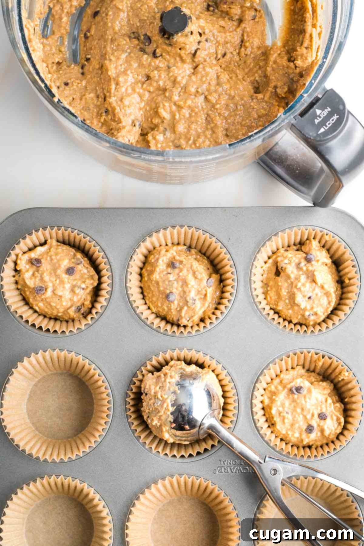 Scooping banana chocolate chip muffin batter evenly into lined muffin tins for baking.