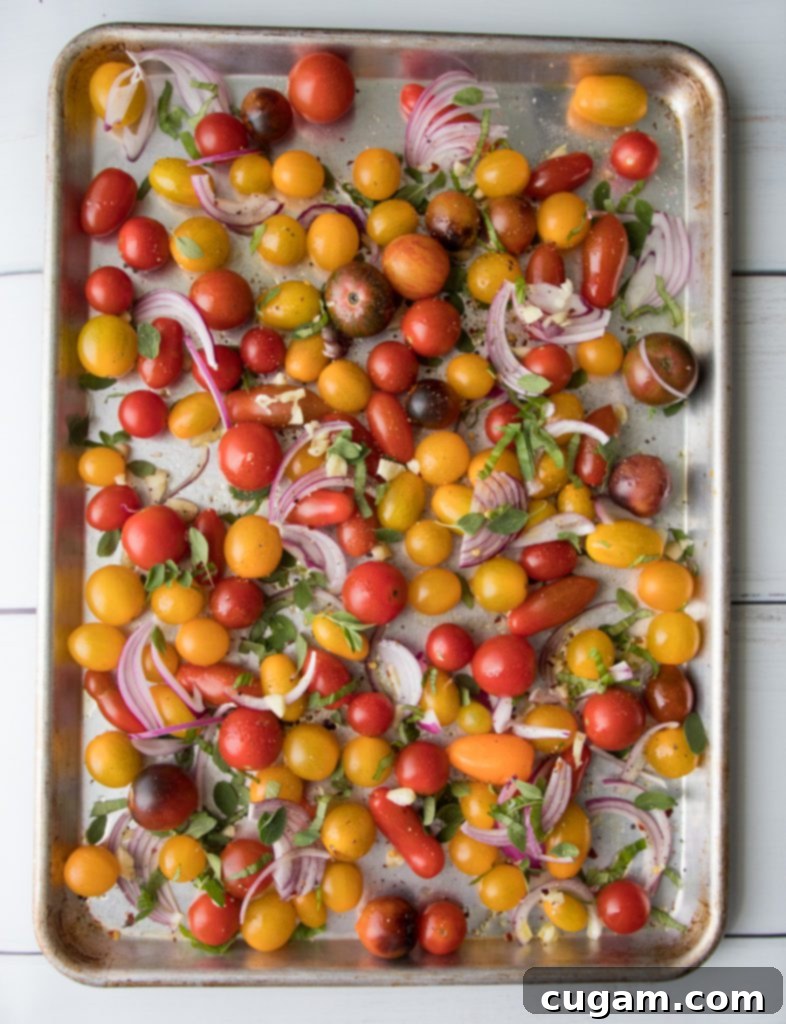 Tomatoes, onions, garlic, and fresh herbs spread out on a baking tray.
