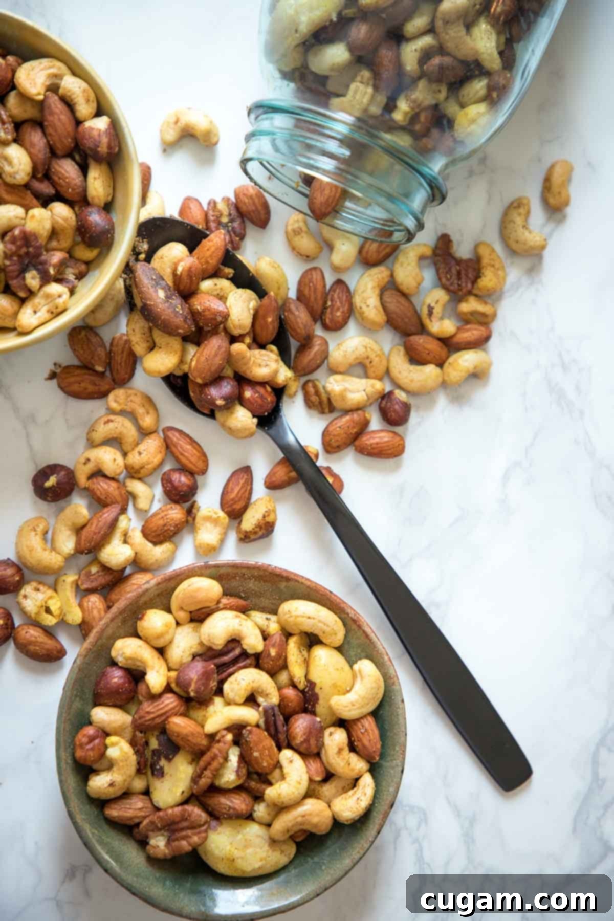 Savory spiced nuts spilling out of a decorative jar and spooned into a rustic bowl, ready for snacking.