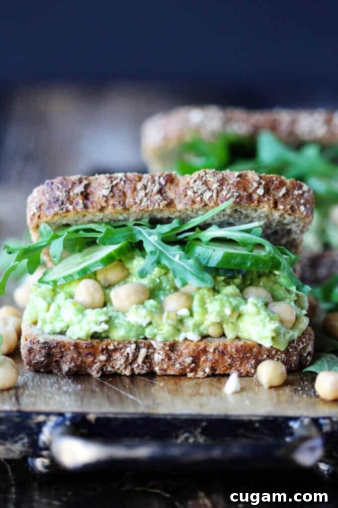 Delicious Smashed Chickpea Avocado Feta Sandwich with cucumber and arugula, served on a rustic wooden board.