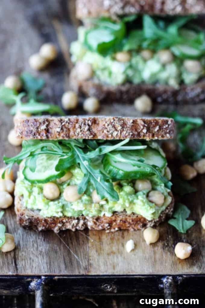 Two freshly prepared Smashed Chickpea Avocado Feta Sandwiches on a wooden board, ready to be served.