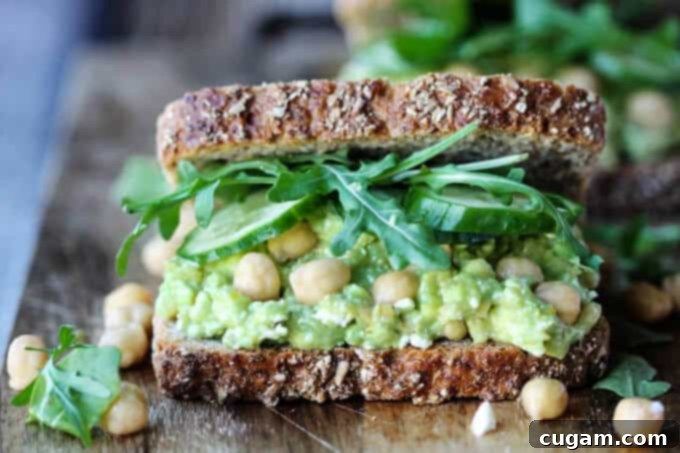 Smashed chickpea avocado feta sandwich cut in half, showcasing its fresh ingredients and creamy filling on a cutting board.