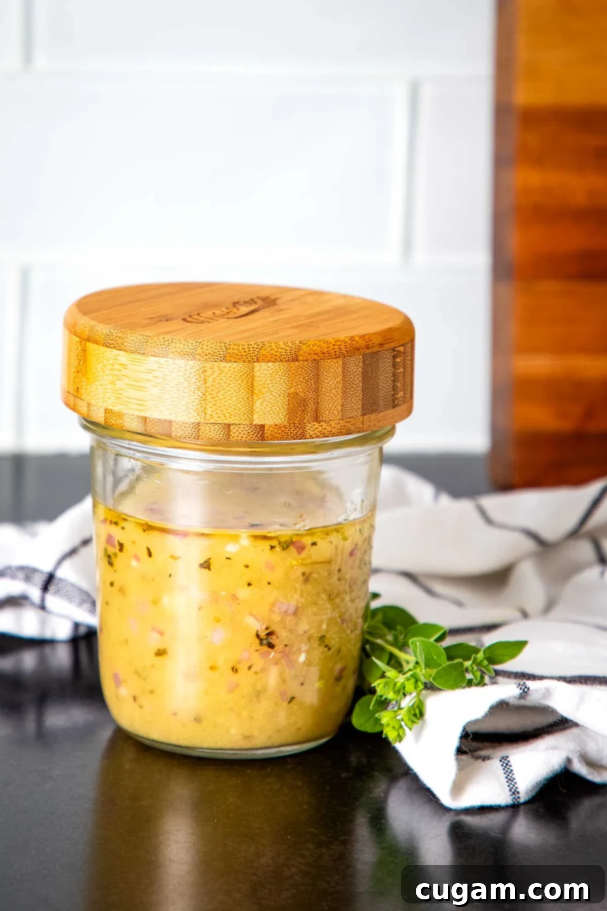 Jar of homemade lemon vinaigrette salad dressing, yellowish with visible minced shallots and herbs, ready to be served.
