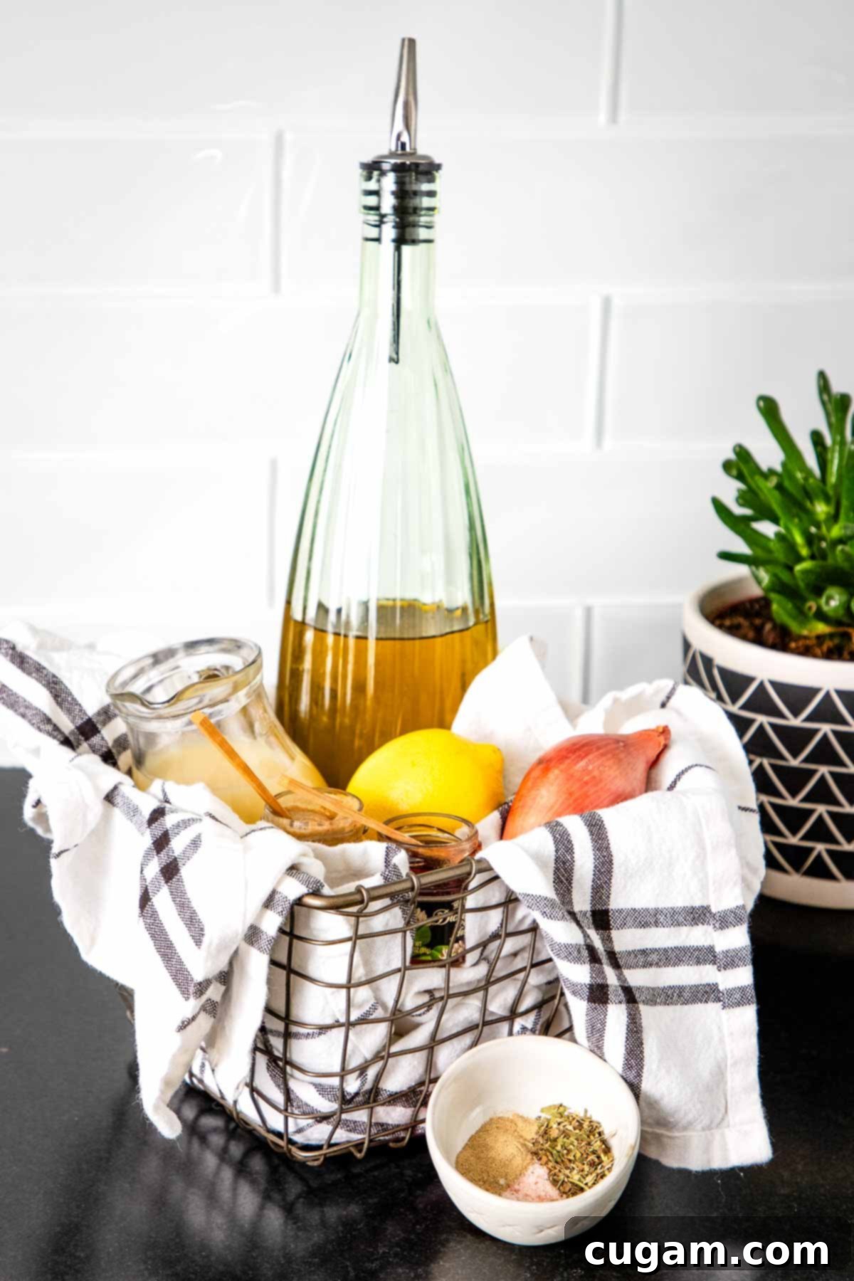Basket containing fresh ingredients for salad dressing: a bottle of olive oil, fresh lemons, a shallot, and sprigs of fresh herbs and spices.